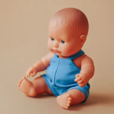 Miniland lėlė berniukas mėlynu kombinezonu (21 cm.) rudame fone