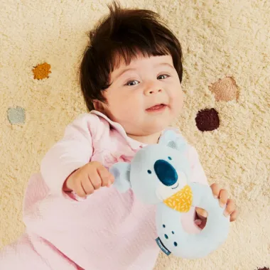 Mergaitė žaidžia su minkštu barškučiu iš Miniland dovanų rinkinio kūdikiams Koala