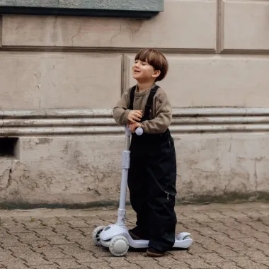 Vaikas stovi šalia levandų spalvos paspirtuko vaikams