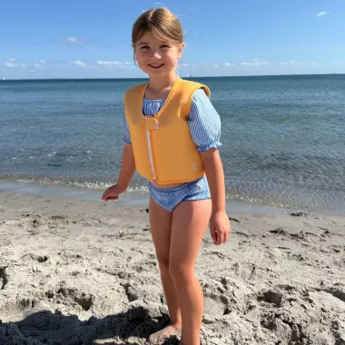 Mergaitė paplūdimyje dėvi plaukimo liemenę vaikams 11–35 kg