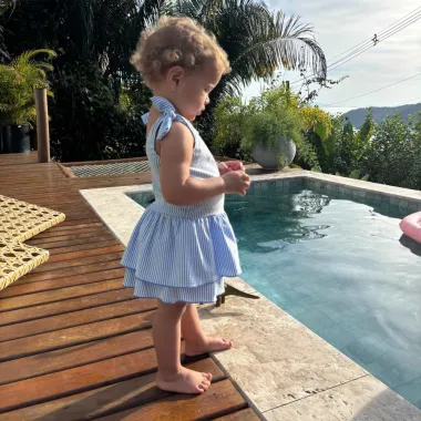 Mergaitei su dryžuotu žydru maudymosi kostiumėliu prie baseino